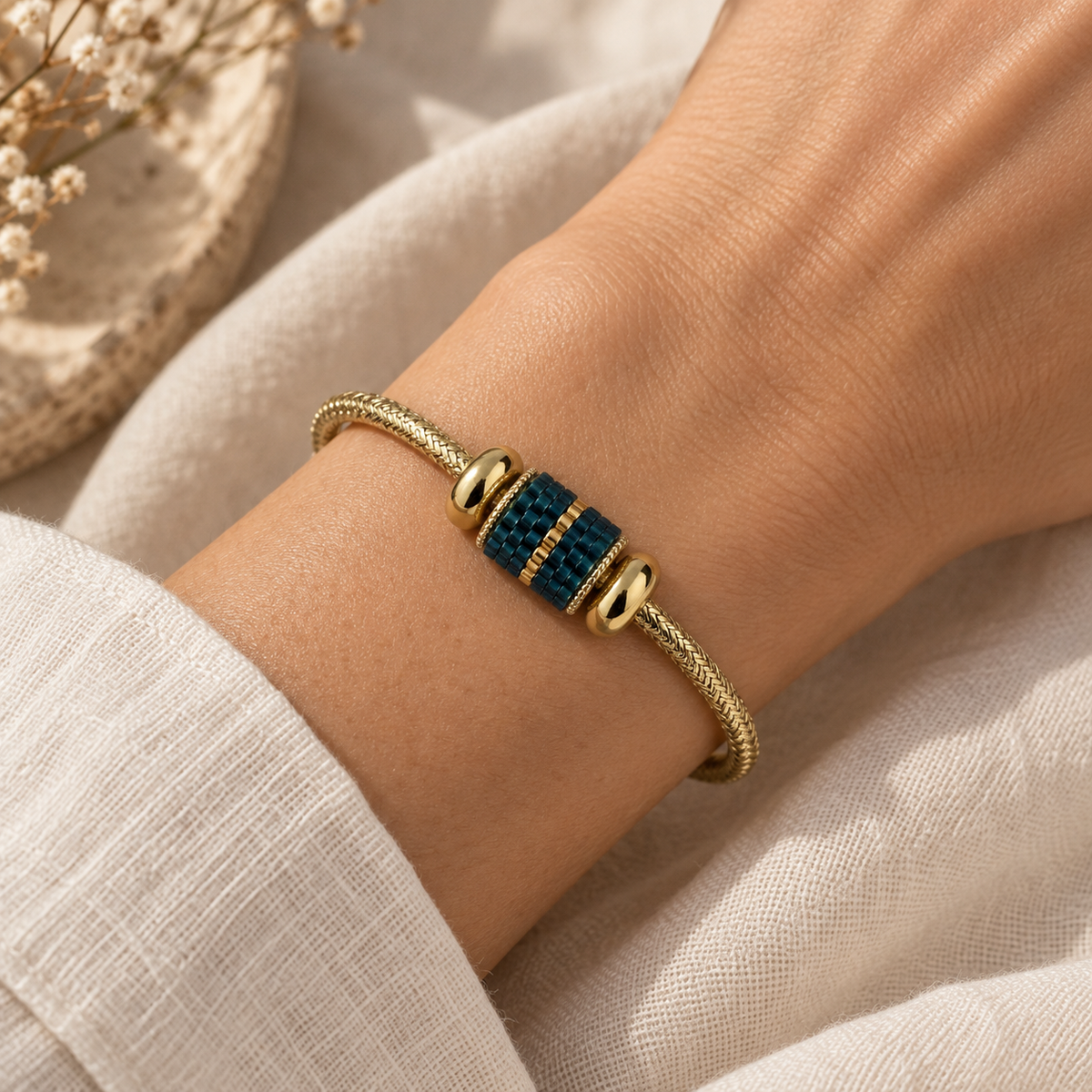 Dark teal and gold beaded cuff bracelet styled on a wrist with cream linen