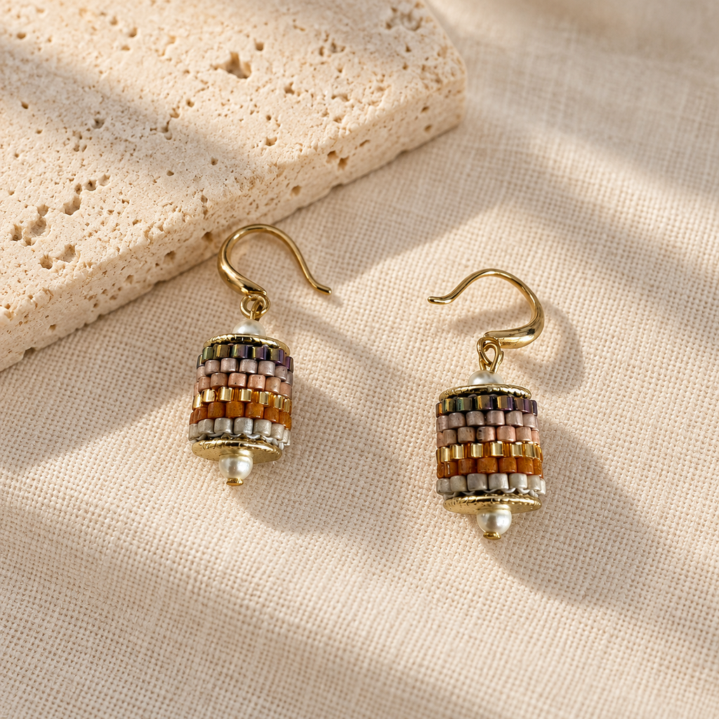 Pair of multicolour beaded drop earrings styled on cream linen beside pale stone