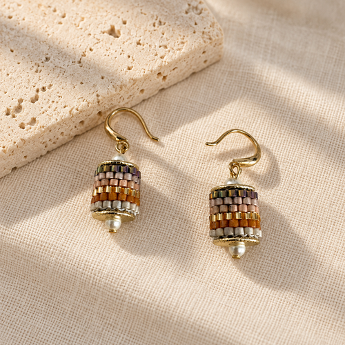 Pair of multicolour beaded drop earrings styled on cream linen beside pale stone
