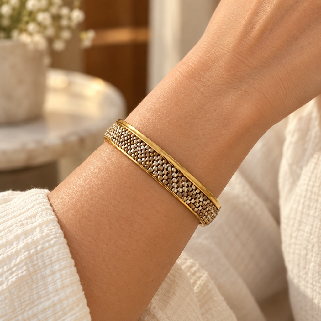 Gold-toned bangle with intricate white, champagne and warm metallic beadwork — styled view