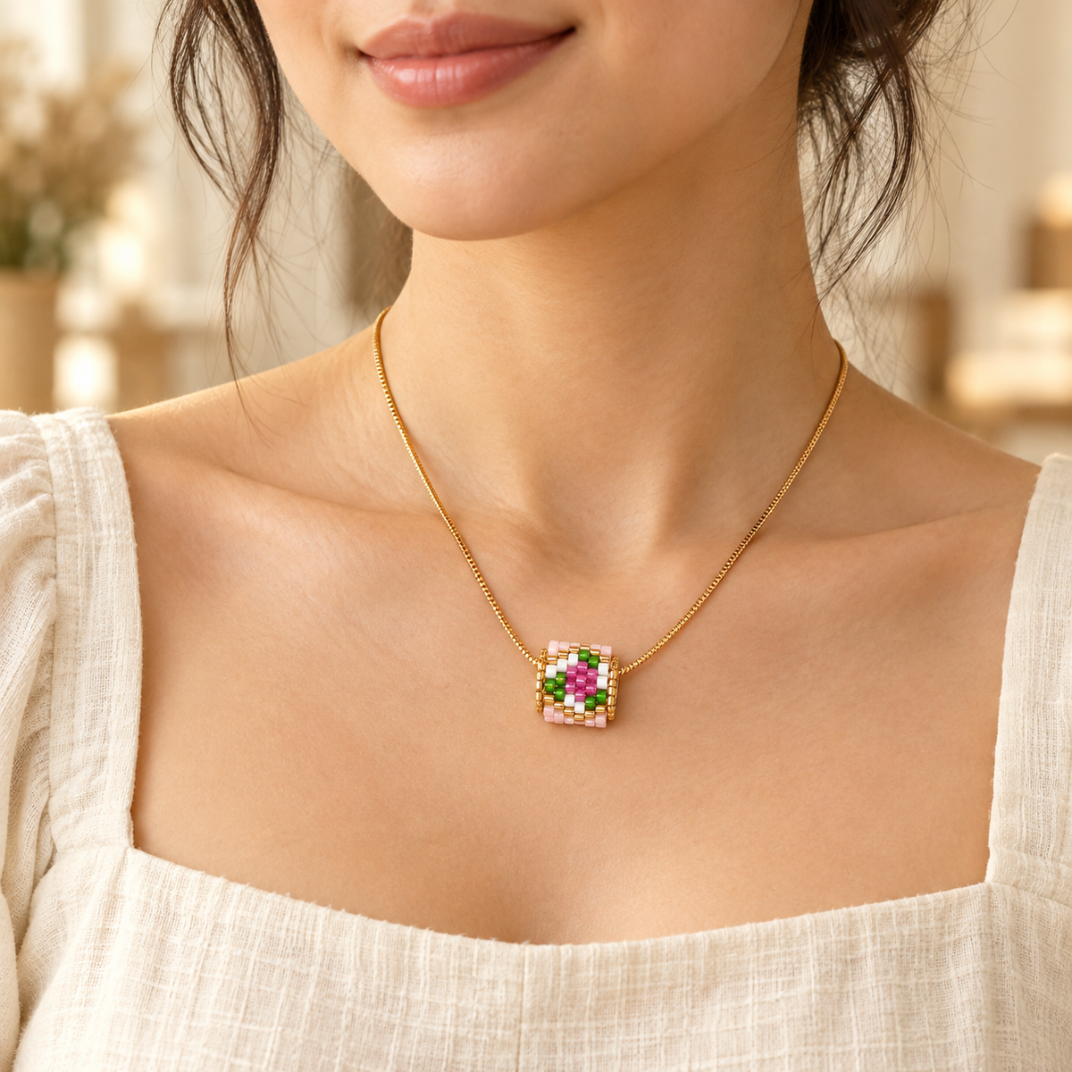 Gold-toned necklace with a pink, green, white and magenta geometric beaded pendant — styled view