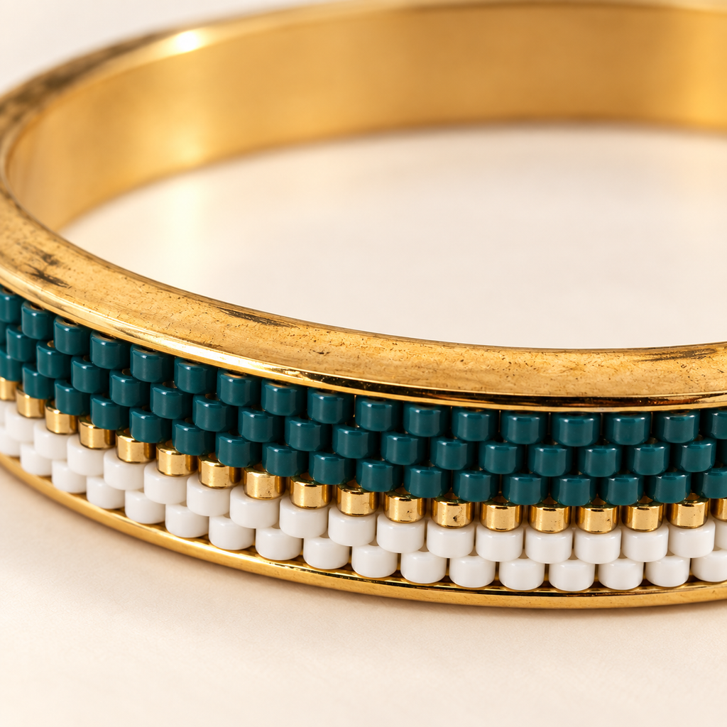Gold-toned bangle with deep teal, white and gold-toned beadwork — close-up detail
