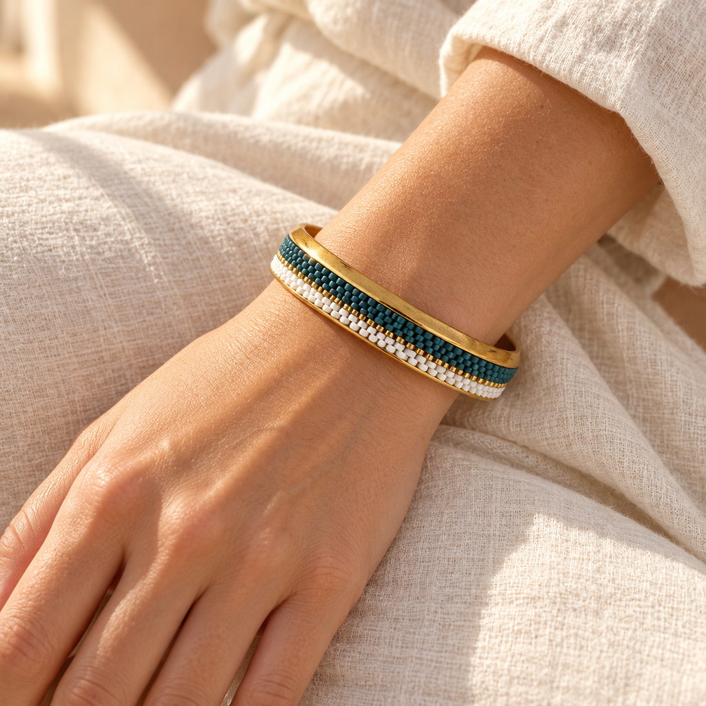 Gold-toned bangle with deep teal, white and gold-toned beadwork — styled view